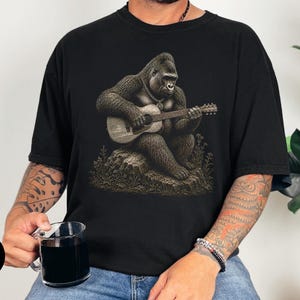 Detailed gorilla playing acoustic guitar while sitting on a rock, vintage engraving artwork for music lovers and guitar players.