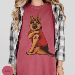 German Shepherd dog illustration wearing a red shirt, lifting sleeve to reveal “I love mom” tattoo, vintage style retro pet graphic, bold clean lines, centered composition, perfect for dog lovers and animal themed apparel designs