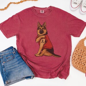 German Shepherd dog illustration wearing a red shirt, lifting sleeve to reveal “I love mom” tattoo, vintage style retro pet graphic, bold clean lines, centered composition, perfect for dog lovers and animal themed apparel designs