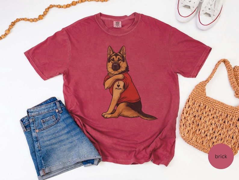 German Shepherd dog illustration wearing a red shirt, lifting sleeve to reveal “I love mom” tattoo, vintage style retro pet graphic, bold clean lines, centered composition, perfect for dog lovers and animal themed apparel designs