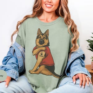 German Shepherd dog illustration wearing a red shirt, lifting sleeve to reveal “I love mom” tattoo, vintage style retro pet graphic, bold clean lines, centered composition, perfect for dog lovers and animal themed apparel designs