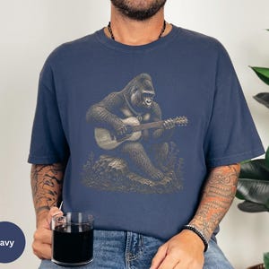 Vintage engraving style gorilla playing an acoustic guitar while seated on a rock, detailed wildlife musician illustration with chain necklace.