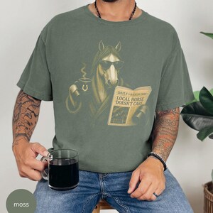 Vintage engraved horse wearing sunglasses and a robe while reading a newspaper and holding a steaming coffee mug. Humorous horse lover design featuring the headline “Local Horse Doesn't Care” in an antique newspaper style. Detailed equestrian artwork with a relaxed, unbothered attitude.