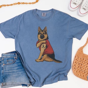 German Shepherd dog illustration wearing a red shirt, lifting sleeve to reveal “I love mom” tattoo, vintage style retro pet graphic, bold clean lines, centered composition, perfect for dog lovers and animal themed apparel designs