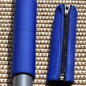 Könnte beinhalten: Zwei zylindrische blaue Abdeckungen aus flexiblem Material. Eine Abdeckung ist um eine Metallstange gewickelt, während die andere abgenommen ist und einen schwarzen vertikalen Reißverschluss in der Mitte mit einem silbernen Metallschieber aufweist.