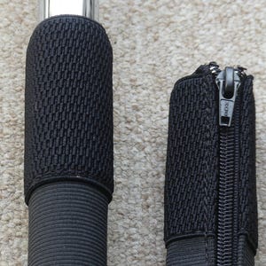 May include: Close-up of a black, textured handle grip and a matching zippered case. The handle grip has a woven pattern and is attached to a silver metal rod. The zippered case has a black zipper and a woven texture.
