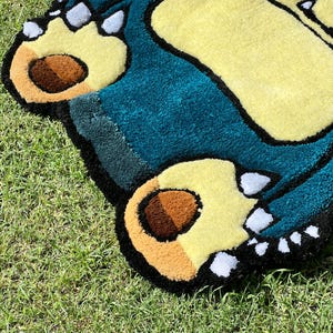 May include: A handmade rug featuring a cartoon character's feet and body. The rug has a teal body, yellow feet, and brown paw pads. The rug is outlined in black and sits on green grass.