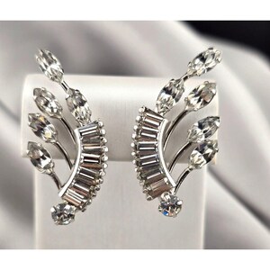 May include: A pair of silver-toned earrings with a floral design. Each earring features a curved row of rectangular crystals and several marquise-cut crystals on delicate stems. A round crystal accents the base of each earring.