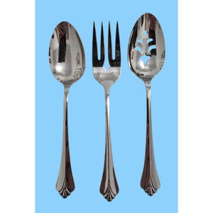 Può includere: Tre posate d'argento: un cucchiaio, una forchetta e un cucchiaio forato. Ogni pezzo ha un manico lungo e sottile con un design decorativo alla base. Lo sfondo è azzurro.