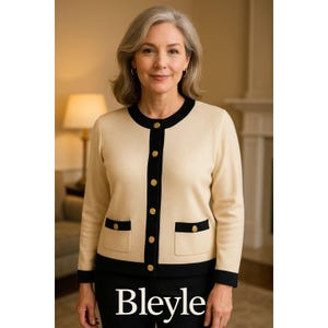 Könnte beinhalten: Ein cremefarbener Cardigan mit schwarzem Besatz, goldenen Knöpfen und Taschen. Der Cardigan wird über einem schwarzen Outfit getragen. Der Markenname "Bleye" ist unten im Bild sichtbar. Der Cardigan ist ein klassischer Stil.