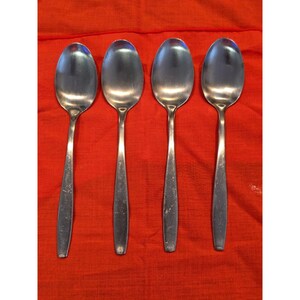 Puede incluir: Cuatro cucharas de acero inoxidable con cuencos ovalados y mangos largos y delgados. Las cucharas están dispuestas sobre una tela roja brillante, creando un contraste entre el metal brillante y el fondo vibrante. Las cucharas son probablemente para comer.