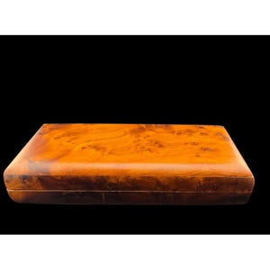 May include: A rectangular wooden box with a polished finish, featuring a prominent burl wood grain pattern in shades of amber, honey, and deep brown. The box has a smooth, glossy surface and a clean, simple design with a visible seam along the side.