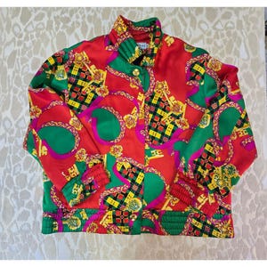 Puede incluir: Chaqueta roja vibrante con un patrón repetido de formas geométricas verdes, amarillas y rosas y diseños dorados en forma de cadena. La chaqueta tiene cuello alto, botones dorados y puños elásticos. Estilo vintage.