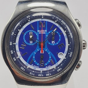 May include: A Swatch chronograph watch with a blue dial and a black leather strap. The watch features a tachymeter scale, three sub-dials, and a date window. The watch face has white and red accents and the text "SWISS".