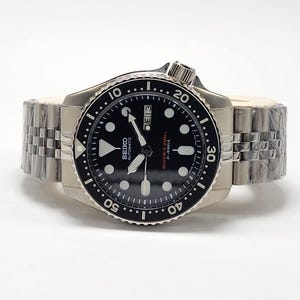 Peut inclure: Montre de plongée automatique Seiko en acier inoxydable avec cadran noir, index lumineux et affichage de la date. La montre est dotée d'une lunette rotative et d'un bracelet en acier inoxydable. Résistante à l'eau jusqu'à 200 mètres.