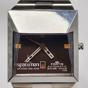 May include: A vintage silver Spaceman Audacieuse watch with a brown face. The watch has a square case and a silver strap. The watch face displays the date and the words "Fortis Automatic Swiss Made T25".