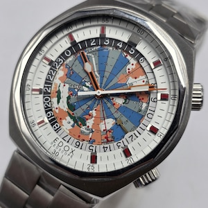 Op de afbeelding: Een roestvrijstalen polshorloge met een witte wijzerplaat met een wereldkaartontwerp in blauw, oranje en groen. Het horloge heeft een zilveren band en de merknaam "EDOX GEOSCOPE" is zichtbaar. De diameter van de wijzerplaat is ongeveer 4 cm.