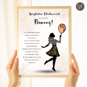 May include: A framed print with German text and a silhouette of a person holding a balloon with the number 10. The print has a light wood frame and is held by two hands.