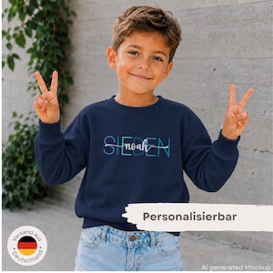 Könnte beinhalten: Ein dunkelblaues Langarm-Sweatshirt mit dem Text SIEDEN in blauen und türkisfarbenen Blockbuchstaben sowie dem Namen noah in weißer Schreibschrift in der Mitte. Das Kleidungsstück wird mit einer hellblauen Jeans kombiniert.