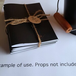 May include: A stack of black notebooks with white edges, tied together with twine and a brown tag that says "Thank You".