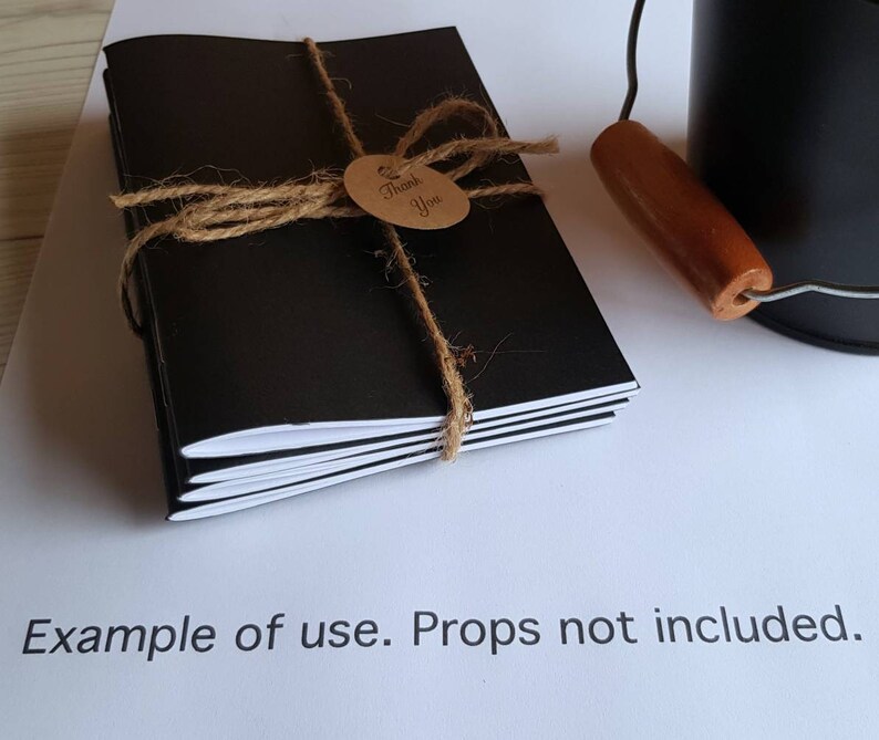 May include: A stack of black notebooks with white edges, tied together with twine and a brown tag that says "Thank You".