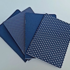 May include: Four blue notebooks with white polka dot patterns. The notebooks are stacked on top of each other.