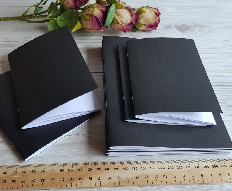 May include: A stack of three black notebooks with white pages. The notebooks are closed and have a smooth, matte finish.