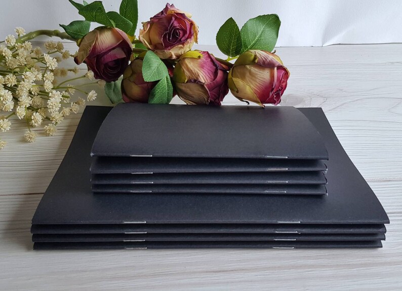 May include: A stack of black notebooks with a simple design. The notebooks are bound with a stitched spine and have a smooth, matte finish.