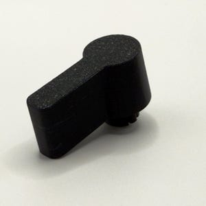 以下が含まれることがあります： 質感のあるマット仕上げの黒いプラスチック製コントロールノブ。このノブは円筒形のベースから長方形のハンドルへと繋がる形状をしており、機械装置や機器のインターフェースを手動で操作するために設計されています。
