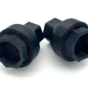 Könnte beinhalten: Zwei schwarze, 3D-gedruckte Radmutternschlüssel. Jeder Schlüssel hat einen sechseckigen Kopf und einen zylindrischen Körper mit strukturierter Oberfläche. Die Schlüssel sind für den Automobilgebrauch bestimmt.