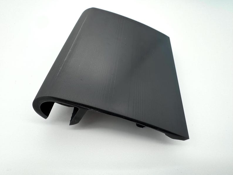 Pode incluir: Uma pe&ccedil;a automotiva de pl&aacute;stico preto com uma superf&iacute;cie texturizada. A pe&ccedil;a tem uma borda curva e uma forma retangular com um ligeiro &acirc;ngulo. &Eacute; provavelmente uma pe&ccedil;a de acabamento ou cobertura para um ve&iacute;culo.