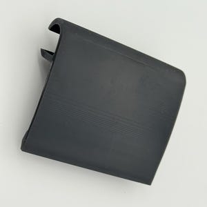 Pode incluir: Um componente de pl&aacute;stico preto, retangular, com uma borda curva e uma superf&iacute;cie ranhurada. O componente tem uma pequena aba saliente em um lado. O objeto est&aacute; sobre um fundo branco.