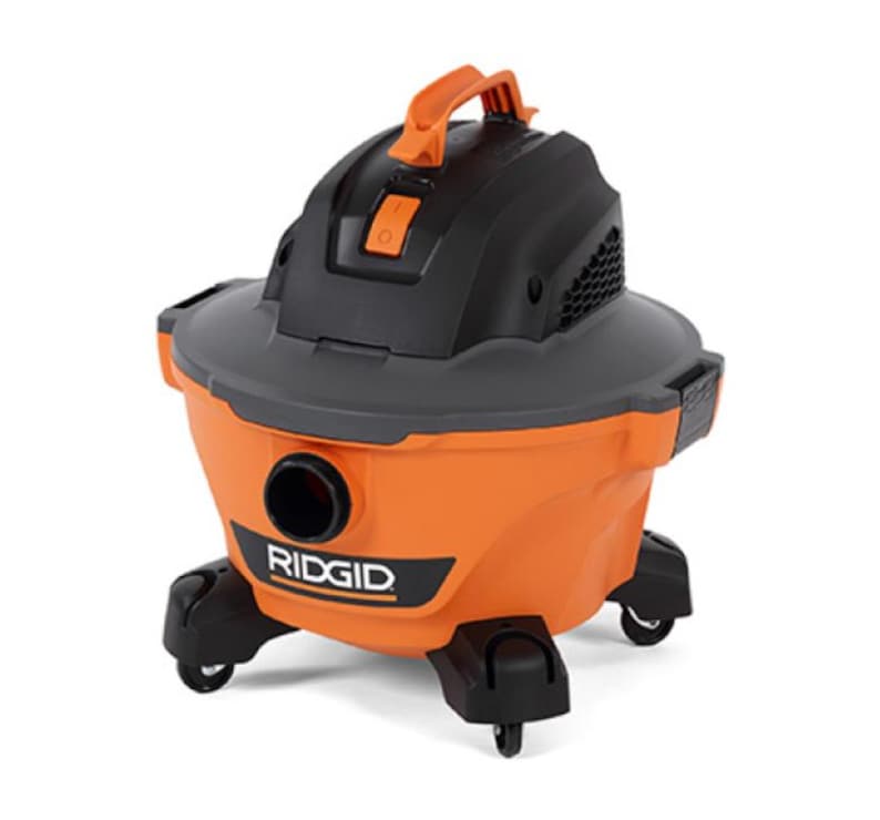 Pode incluir: Um aspirador de p&oacute; e l&iacute;quido RIDGID laranja e preto com uma al&ccedil;a e rodas pretas. O aspirador tem uma parte superior preta e uma abertura redonda para a mangueira. O logotipo RIDGID &eacute; vis&iacute;vel na frente.