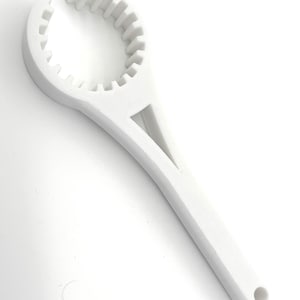 Puede incluir: Un abridor de tarros de plástico blanco con un agarre circular dentado y un mango largo. El mango tiene un recorte triangular y un agujero en el extremo. La herramienta está diseñada para ayudar a abrir tarros y botellas.