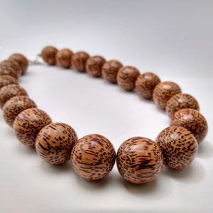 May include: A brown wooden necklace with round beads. The beads have a dark brown and light brown patterned design.