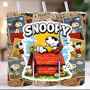 May include: A cylindrical tumbler with a clear straw featuring a collage of Snoopy and Woodstock illustrations. The design includes a central graphic of Snoopy wearing sunglasses on a red doghouse, with vintage newspaper clippings and the text SNOOPY.