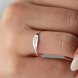 May include: A silver ring with a floral design on the face. The ring is oval-shaped and sits on a finger. The ring is a delicate piece of jewellery.
