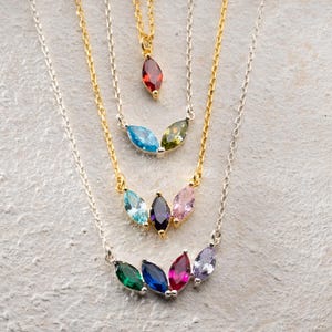 May include: A collection of delicate necklaces with colorful gemstone pendants. The necklaces feature gold and silver chains, each adorned with a different arrangement of marquise-cut stones in various colors, including red, blue, green, and purple.