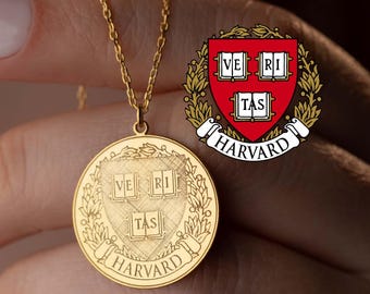 May include: A gold-colored pendant necklace featuring the Harvard University crest. The round pendant displays the university's motto, "Veritas," and the word "Harvard." The necklace is suspended from a delicate chain.