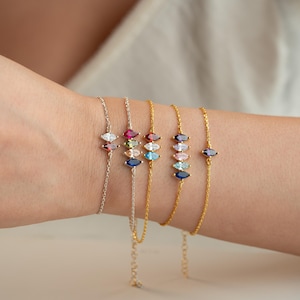 May include: A collection of delicate bracelets with colorful marquise-cut gemstones. The bracelets feature silver and gold chains, each adorned with a row of vibrant stones in various colors, including red, blue, and pink.