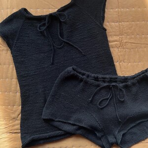 Puede incluir: Un conjunto de dormir negro tejido, que consta de una camiseta de manga corta con un lazo en el escote y pantalones cortos a juego con cintura con cordón. El conjunto está hecho de tejido de punto texturizado.