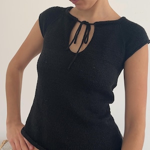 May include: Black knit top with a keyhole neckline and short sleeves. The top features a tie detail at the neckline and a textured knit pattern. The garment is a solid black color.