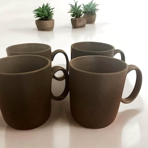 May include: Four brown ceramic mugs with handles. The mugs are arranged in a square shape on a white surface.