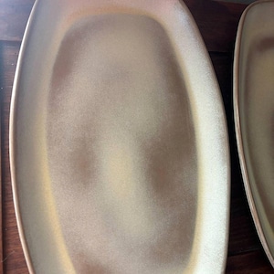 May include: Two oval-shaped serving platters with a matte, speckled finish. The platters have a light beige color with a slightly darker rim. The shape is elongated with rounded corners, suitable for serving appetizers or entrees.