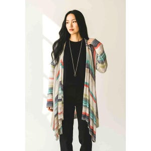 May include: A long, open-front cardigan with a striped pattern in shades of beige, blue, orange, and green. The cardigan is worn over a black top and pants. A silver necklace with a circular pendant is also visible.
