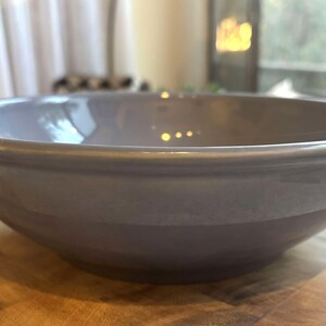 Puede incluir: Un cuenco grande y redondo de cerámica gris con acabado brillante. El cuenco se encuentra sobre una superficie de madera y tiene un borde ancho. Ideal para servir ensaladas, pasta u otros platos. Una pieza sencilla pero elegante para la cocina.