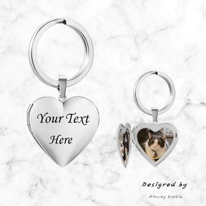May include: A silver heart-shaped locket keychain with a photo inside. The locket is open, revealing a picture of a cat. The text "Your Text Here" is on the closed locket. The words "Designed by Ainsley Sophia" are also visible.