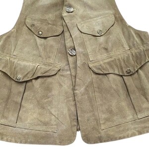 Peut inclure: Un gilet en daim beige avec quatre poches avant et des fermetures boutonn&eacute;es. Le gilet a un design classique avec un aspect l&eacute;g&egrave;rement us&eacute;. Les poches ont des rabats boutonn&eacute;s. Le gilet est de couleur neutre.