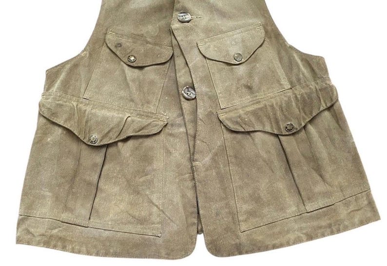 Peut inclure: Un gilet en daim beige avec quatre poches avant et des fermetures boutonn&eacute;es. Le gilet a un design classique avec un aspect l&eacute;g&egrave;rement us&eacute;. Les poches ont des rabats boutonn&eacute;s. Le gilet est de couleur neutre.