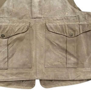 Peut inclure: Gros plan d'un gilet beige avec deux grandes poches avant et deux poches plus petites. Le gilet a un aspect vieilli, avec une texture visible et de l&eacute;g&egrave;res variations de couleur. Les poches sont fix&eacute;es par de petits boutons ronds.